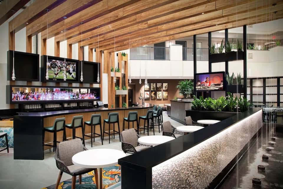 Modern hotel bar and lounge with wooden beams, black bar counter, and multiple seating areas