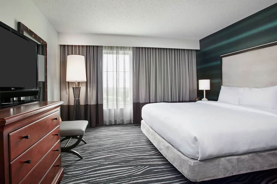 Modern hotel bedroom with queen bed, dark teal accent wall, and balcony access