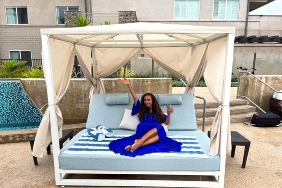 Woman lounging on blue canopy daybed by pool at resort rooftop