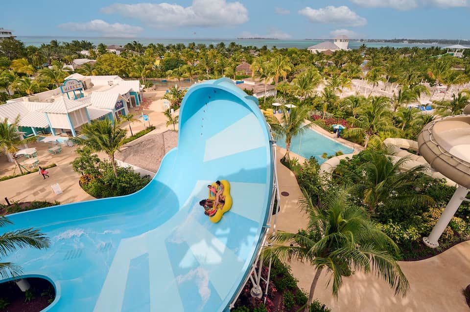 Aerial view of water park with blue slide, pools, palm trees, and surrounding facilities