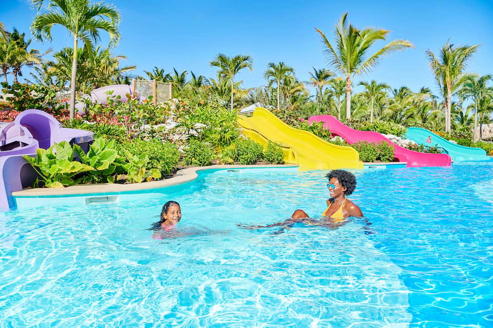 Family-friendly resort pool with colorful water slides, palm trees, and children swimming