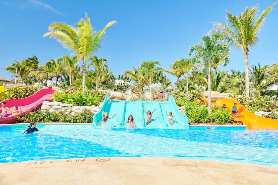 Family water park with colorful slides and children playing in bright blue pool