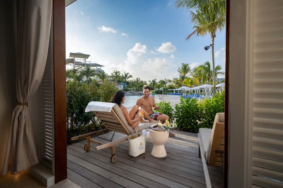 Couple relaxing on a waterfront deck with lounge chairs overlooking a tropical resort landscape