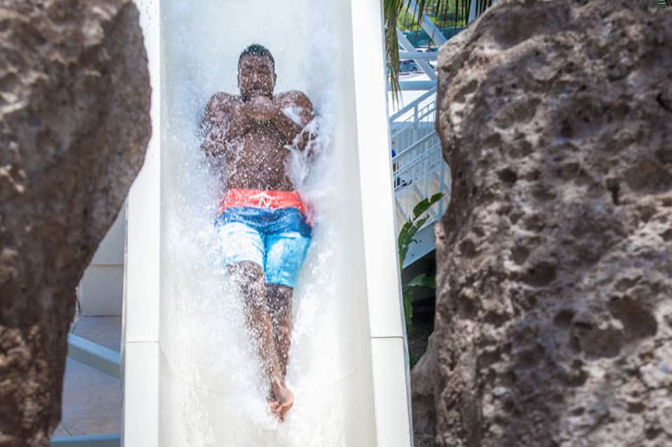 Person sliding down white water slide between rock formations at tropical resort