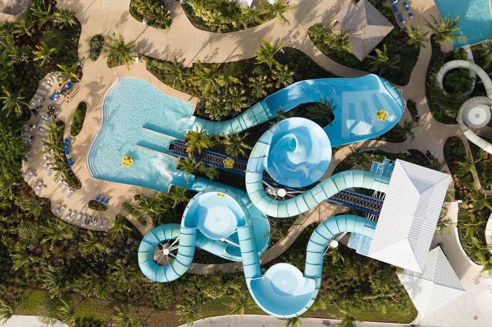 Aerial view of resort water park with blue slides, lazy river, pools, and tropical landscaping