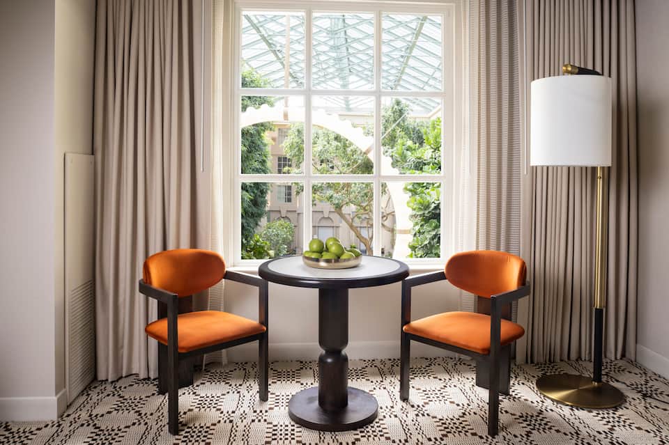 Elegant seating nook with orange velvet chairs, round black table, and large windows overlooking trees