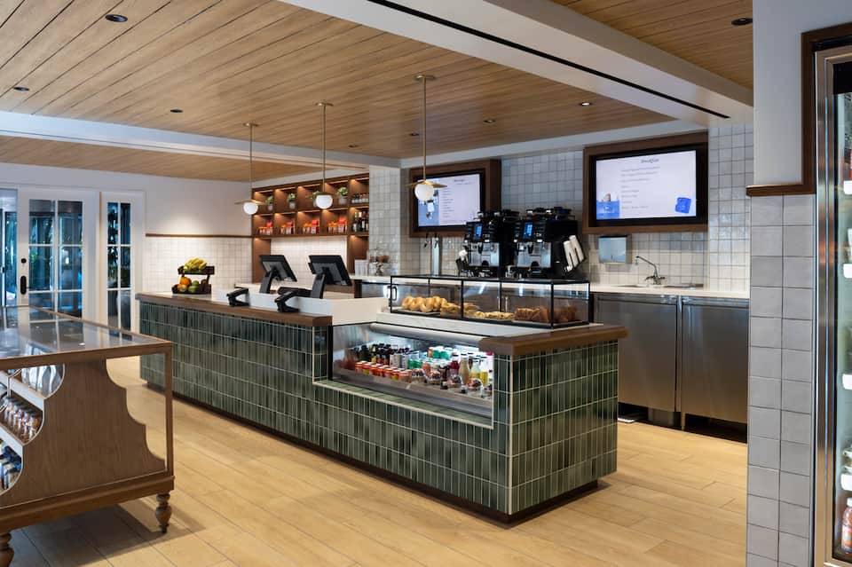 Contemporary hotel café with white tile walls, wood ceiling, espresso bar, and digital menu displays