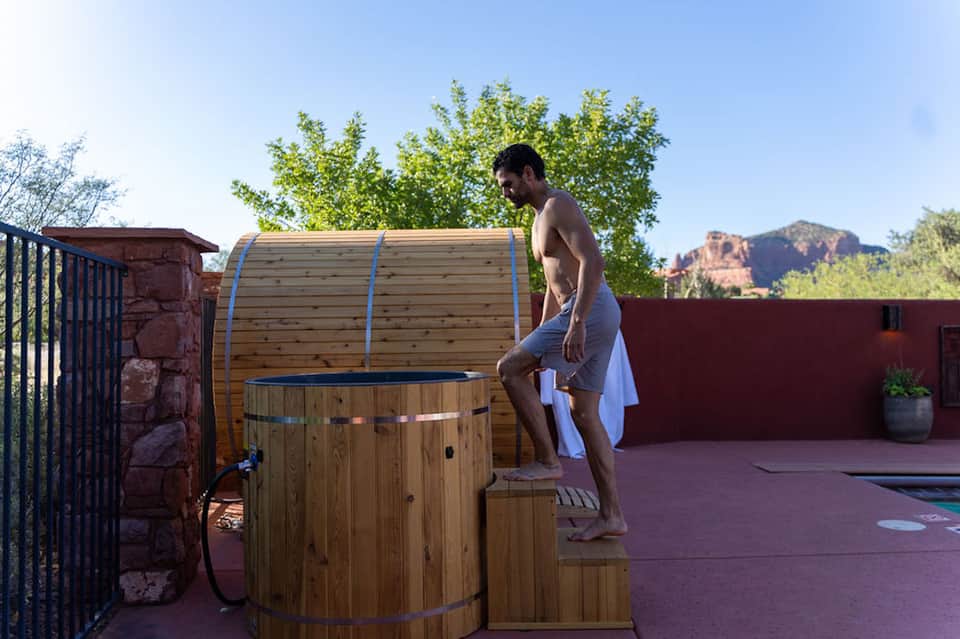 Man about to enter wooden hot tub on terrace with red rocks and mountains in background