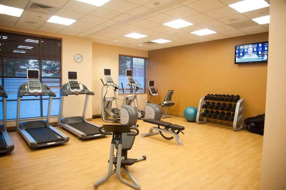 Fitness center with treadmills, exercise bikes, weights, and equipment under bright ceiling lights