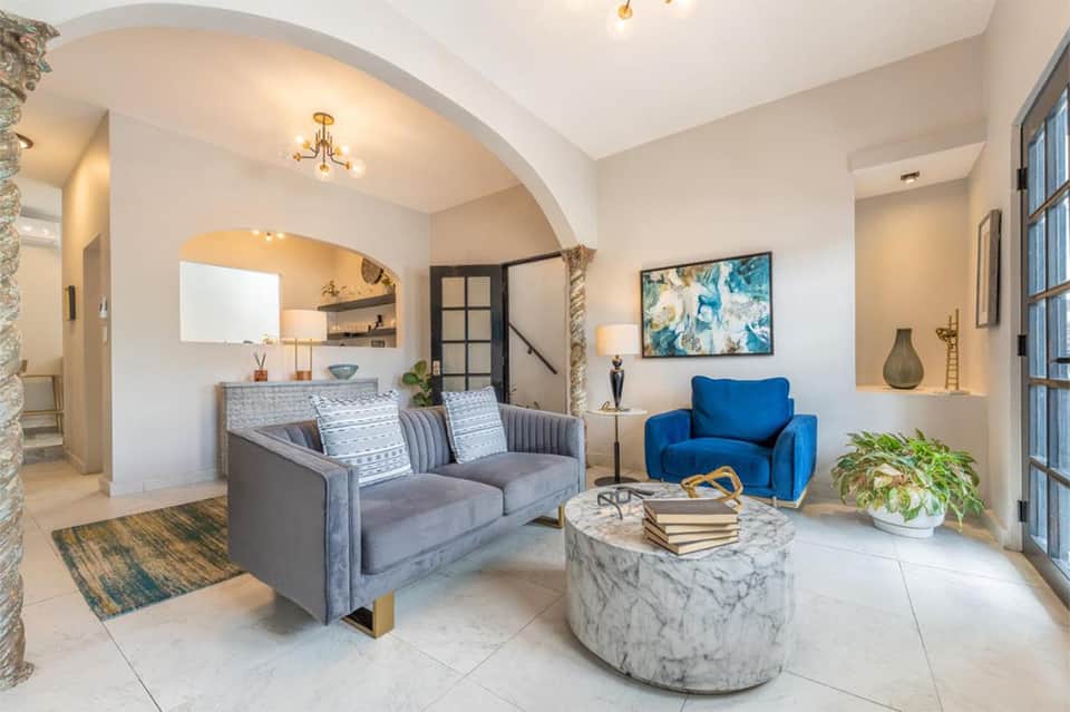 Modern residential lobby with arched ceiling, gray sofa, blue chair, and marble coffee table