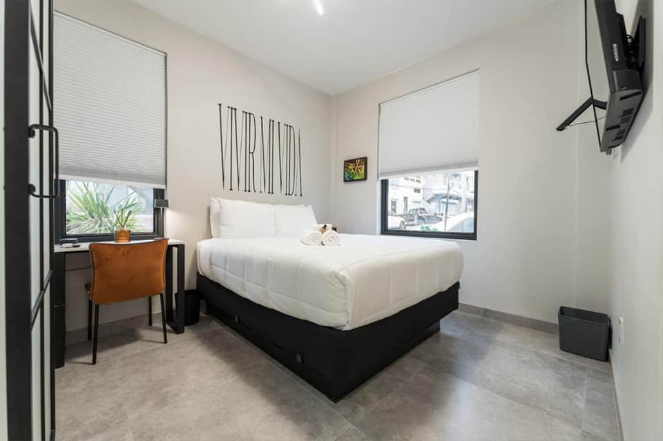 Minimalist hotel bedroom with white bedding, small desk, and window views