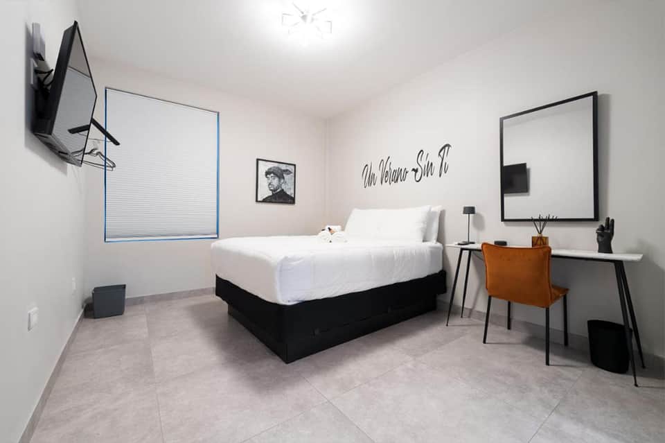 Minimalist hotel room with white bed, desk, flat-screen TV, and contemporary artwork on wall