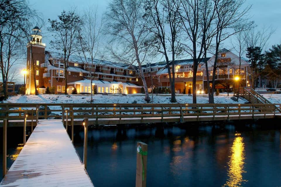 Riverside hotel exterior in winter with snow, lit windows, wooden dock at evening