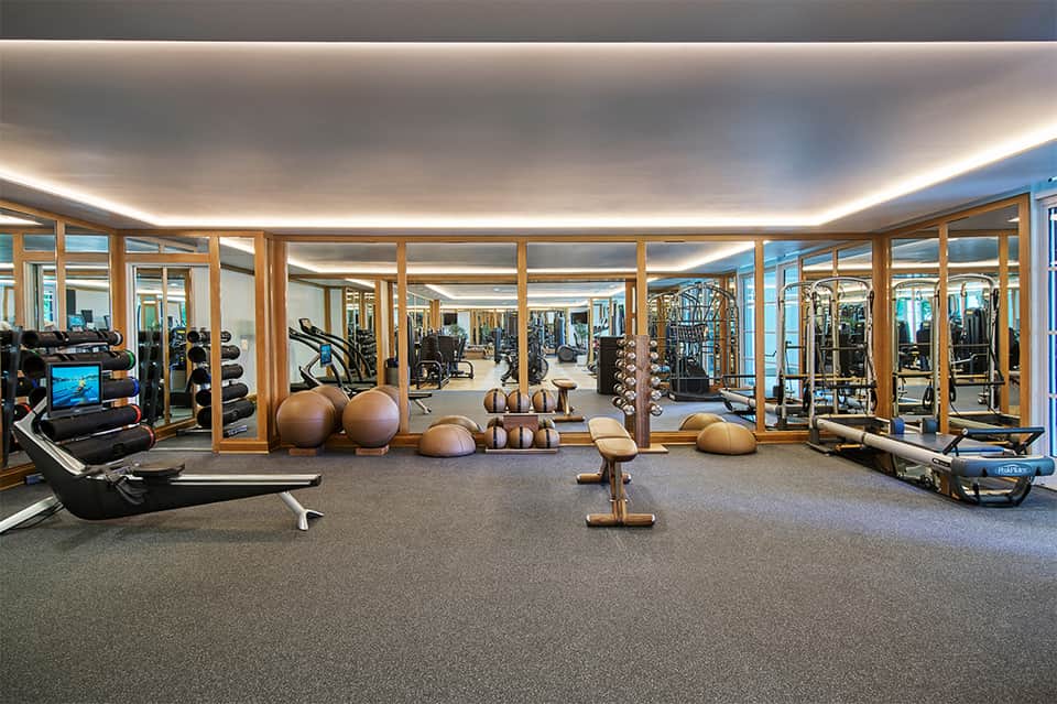 Modern gym with cardio machines, exercise balls, free weights, and mirror-lined walls with wood accents