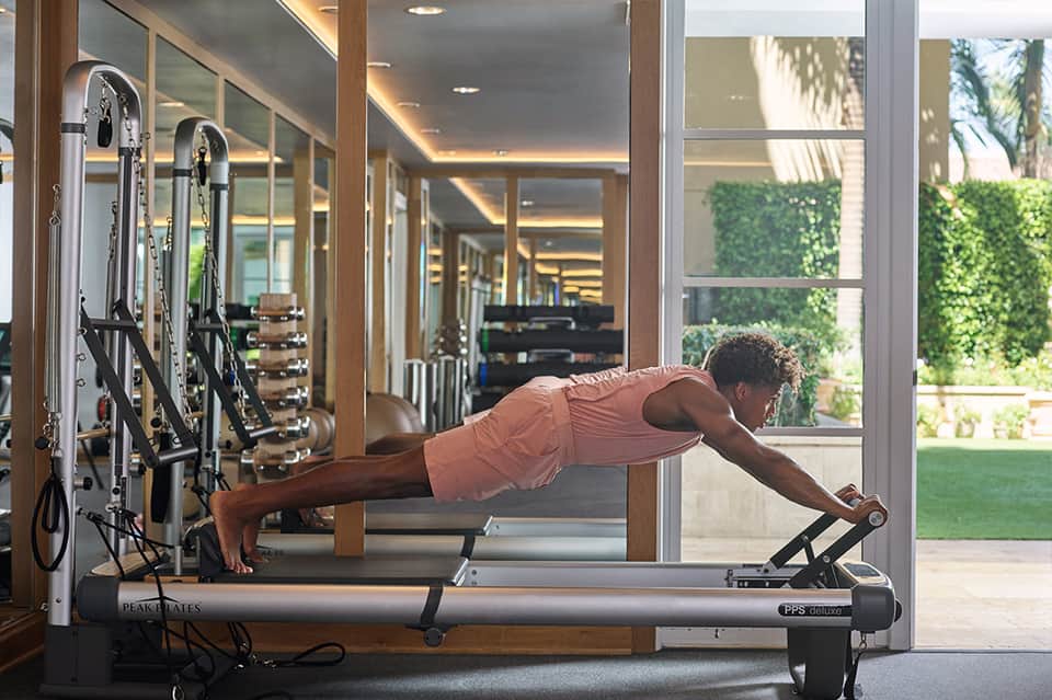 Man performing plank exercise on Pilates reformer machine in bright fitness studio with garden view