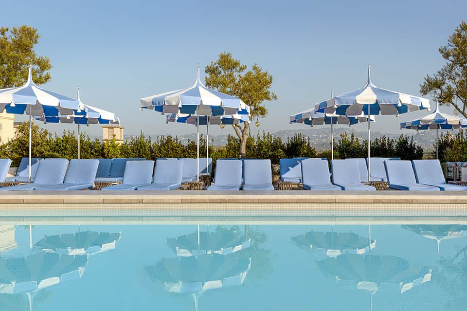 Resort pool with blue and white striped umbrellas, white lounge chairs, and mountain views in background
