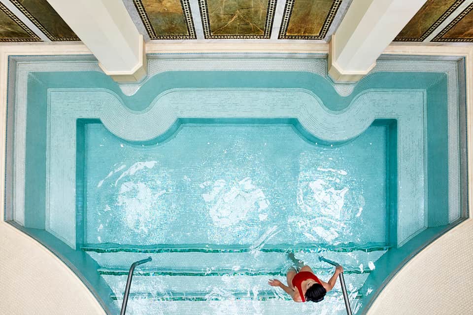 Overhead view of indoor pool with decorative tile mosaic and swimmer in red doing backstroke