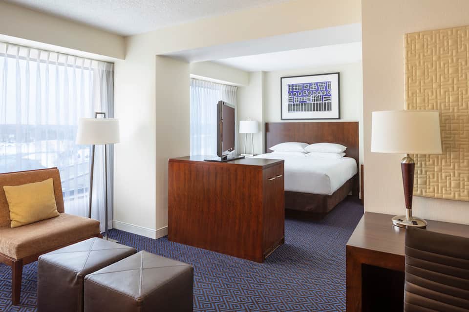 Hotel suite with bedroom, living area, dark wood furniture, and ocean-view windows