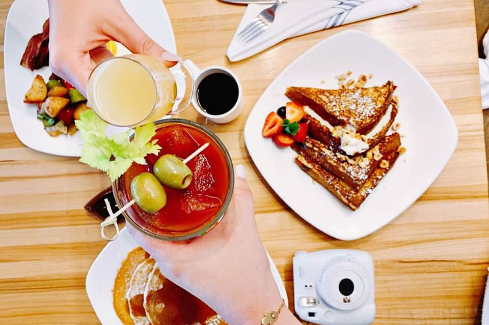 Overhead view of brunch spread with French toast, cocktails, and pastries on wooden table