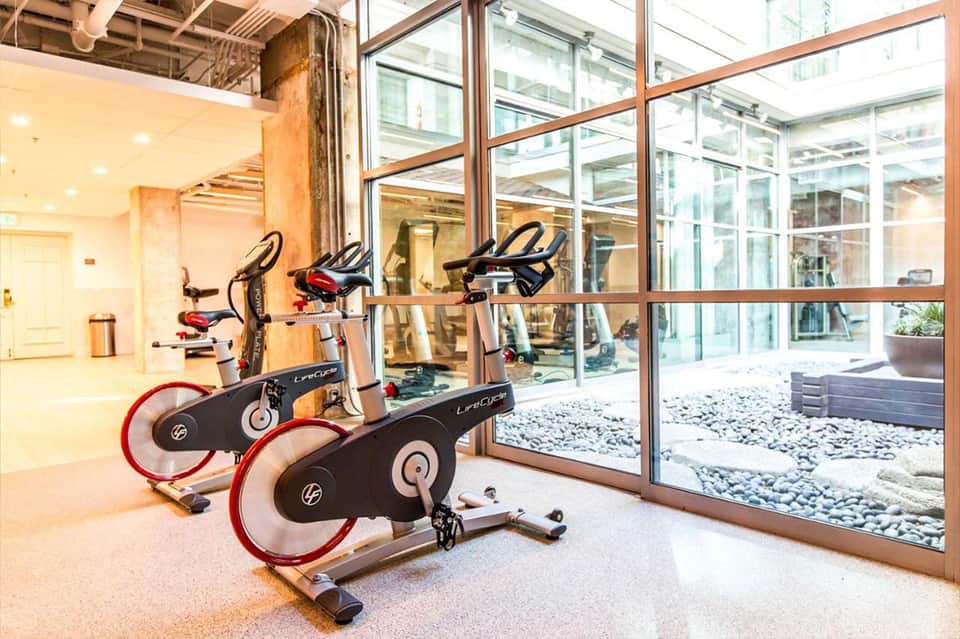 Contemporary fitness studio with stationary bikes, large windows, glass doors, and wooden shelving