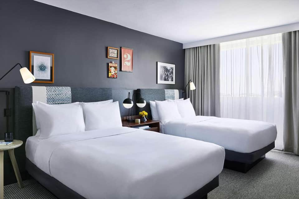 Hotel guest room with two queen beds, gray headboard, modern lighting, and ocean view windows