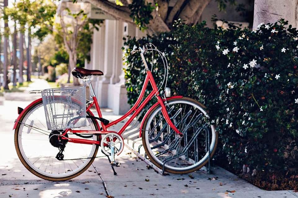 Red vintage bicycle with basket parked on sidewalk next to flowering ivy-covered wall