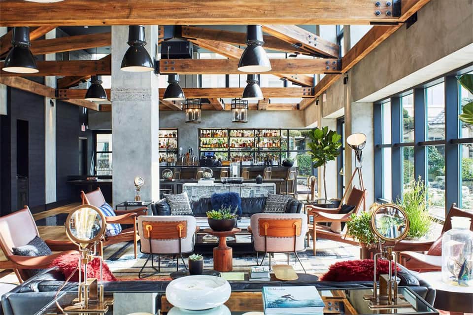 Contemporary resort lobby with exposed wooden beams, leather seating, black pendant lights, and multiple bar areas