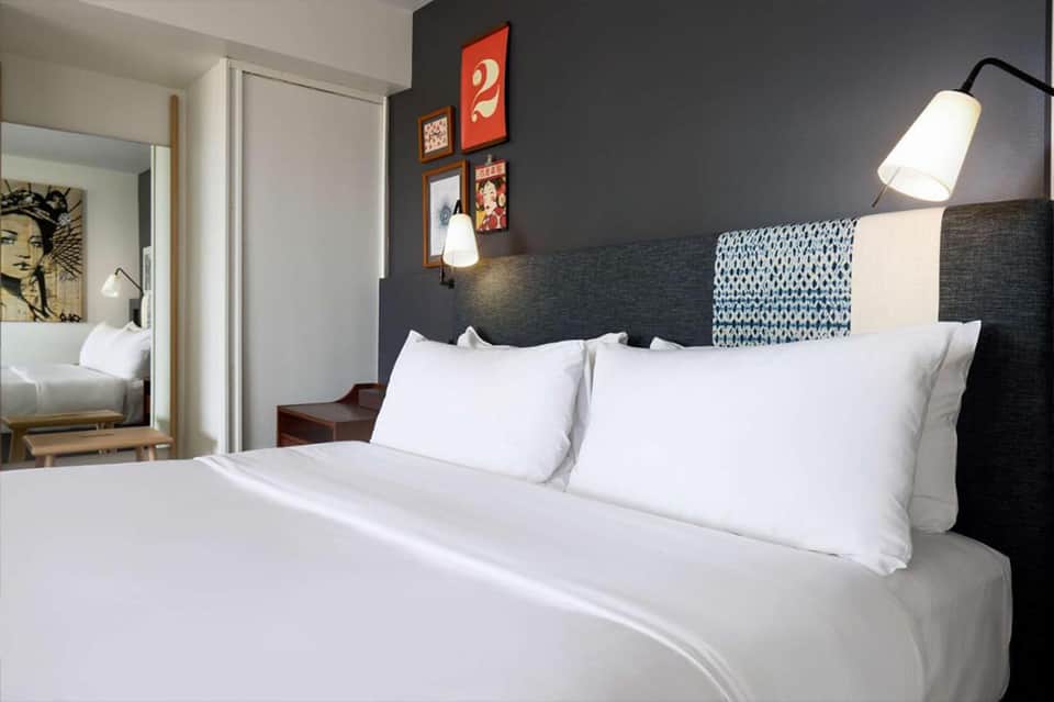 Hotel bedroom with dark accent wall, white bedding, pendant lamps, and ensuite bathroom visible through doorway