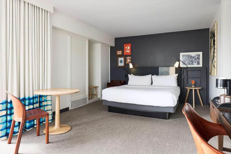 Contemporary hotel bedroom with dark accent wall, white bedding, and mid-century modern furnishings