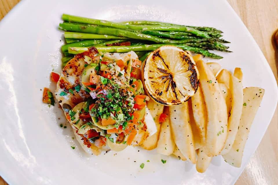 Grilled fish fillet with asparagus, roasted potatoes, and lemon garnish on white plate