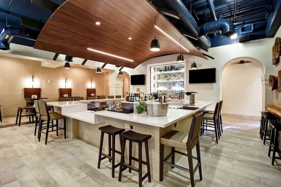 Modern bar and lounge with wooden ceiling, white marble countertop, pendant lighting, and dark wood furnishings