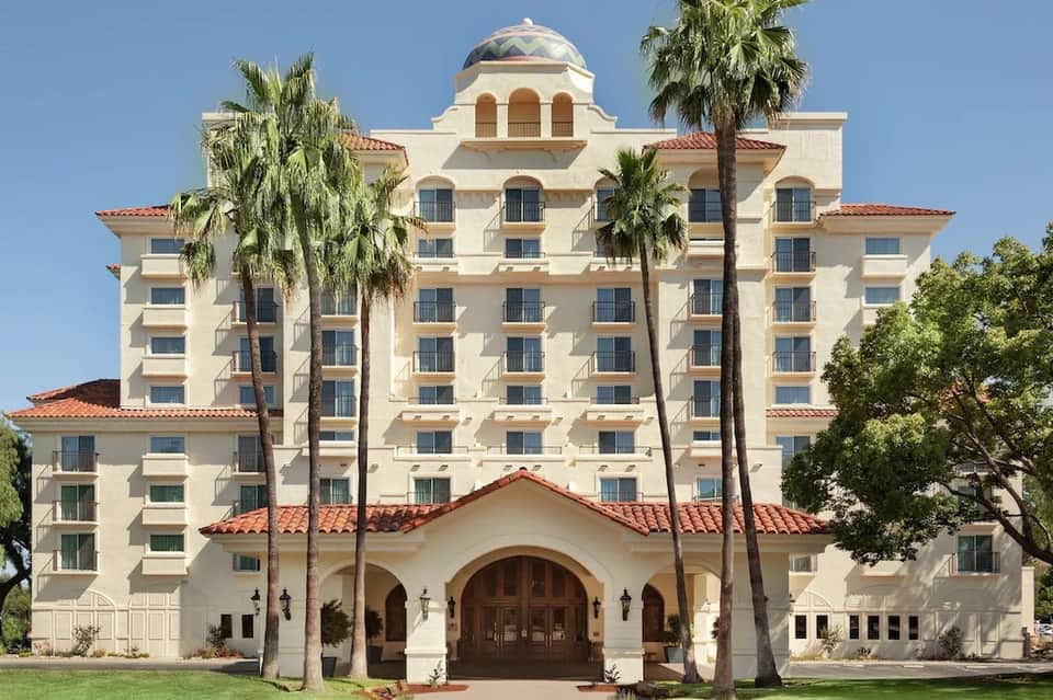 Historic white hotel building with red tile roof, palm trees, and domed cupola against blue sky