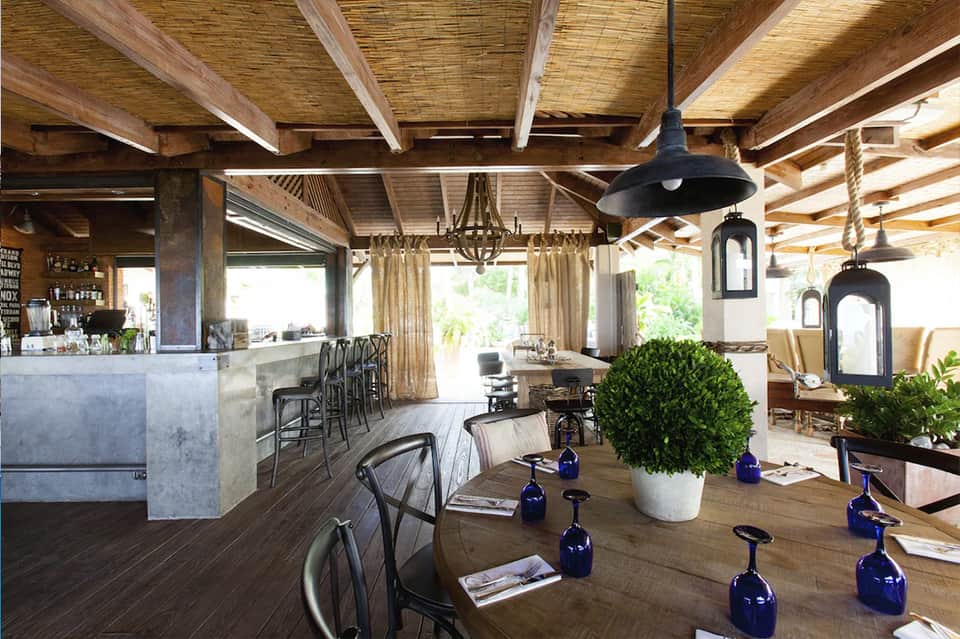 Modern resort restaurant and bar with wooden ceiling beams, black pendant lights, and ocean view access