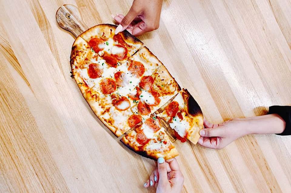 Hands sharing a pepperoni pizza on a wooden board