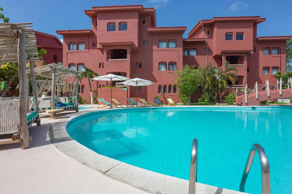 Large turquoise pool with red-orange hotel buildings, umbrellas, and lounge chairs