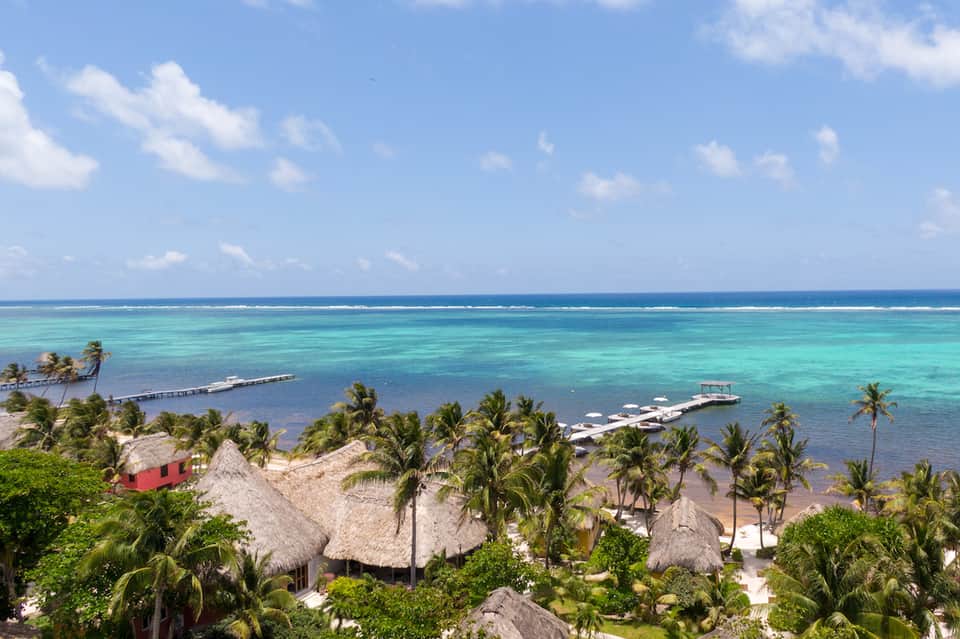 Aerial view of tropical beach resort with thatched-roof structures, palm trees, and turquoise water