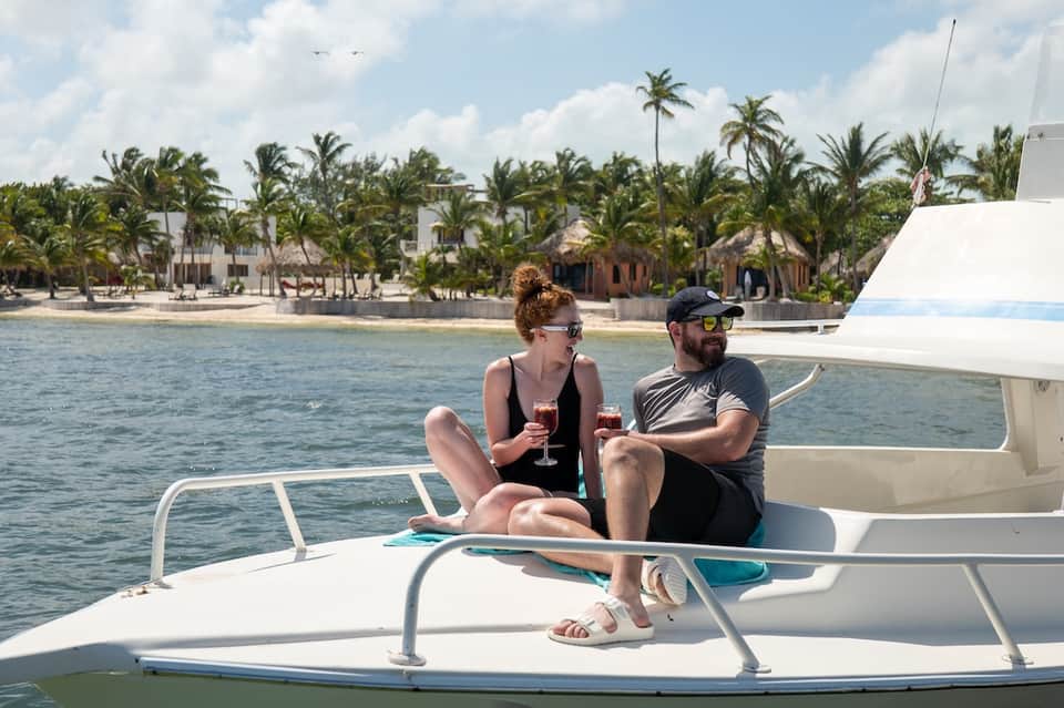 Couple enjoying drinks on a boat with palm-lined beach resort visible in background