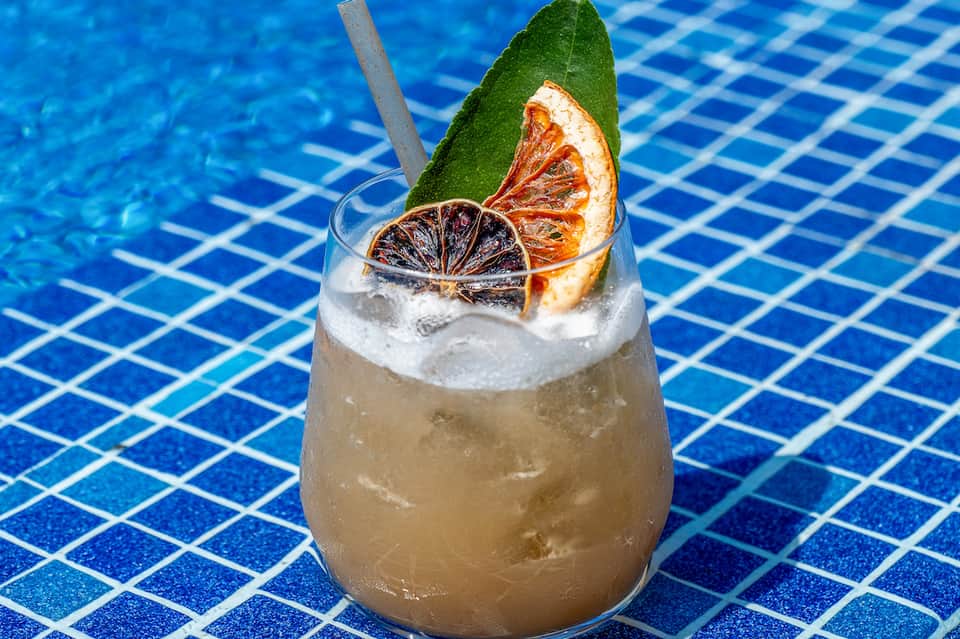 Refreshing cocktail with citrus garnish and mint leaf floating in blue pool water