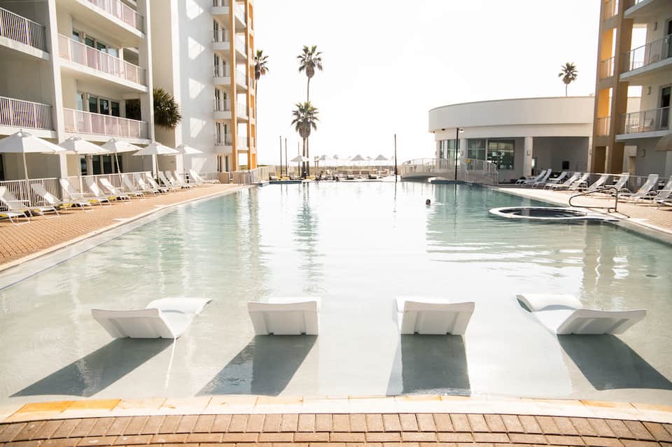 Resort pool with lounge chairs, palm trees, and modern residential buildings