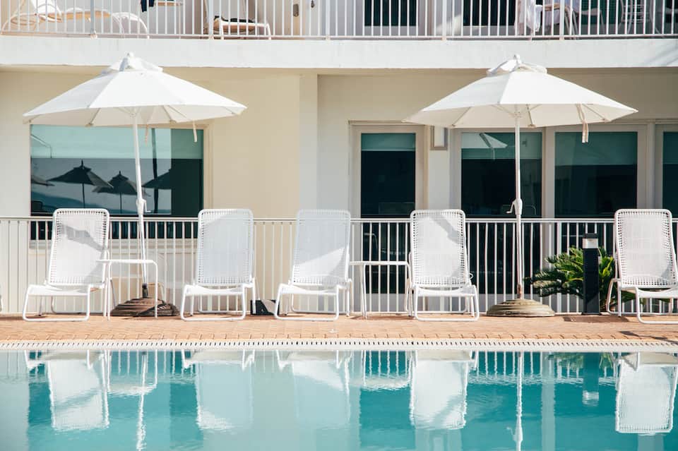 Poolside lounge area with white chairs, umbrellas, and reflecting water at modern resort