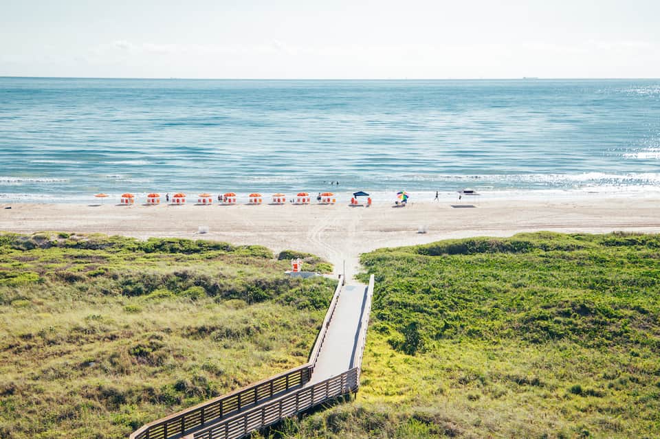 Beach access with wooden boardwalk, sandy shore, striped umbrellas, and ocean horizon