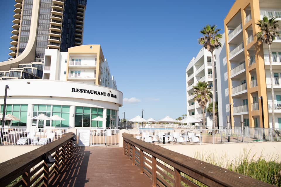 Beachfront resort with modern yellow and white apartment buildings, sandy beach area, and wooden boardwalk