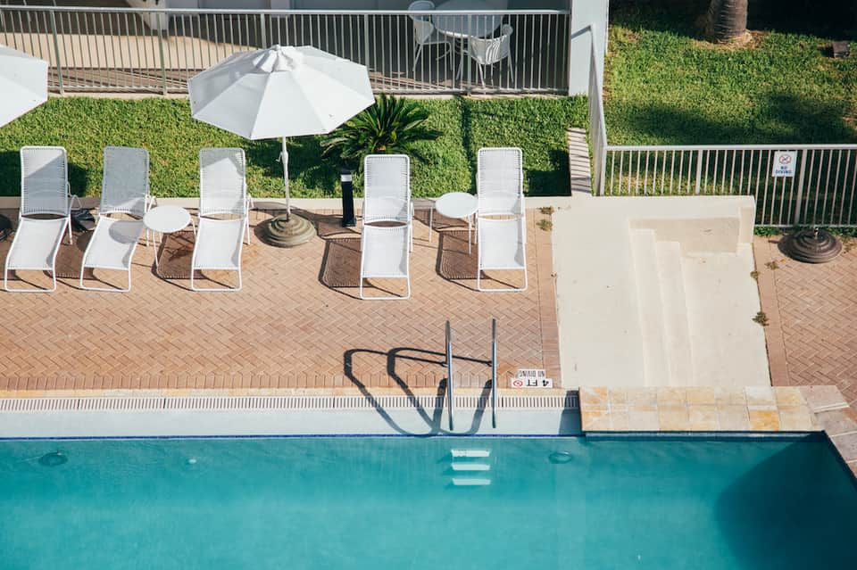 Outdoor pool deck with white lounge chairs, white umbrella, green lawn, and metal railings