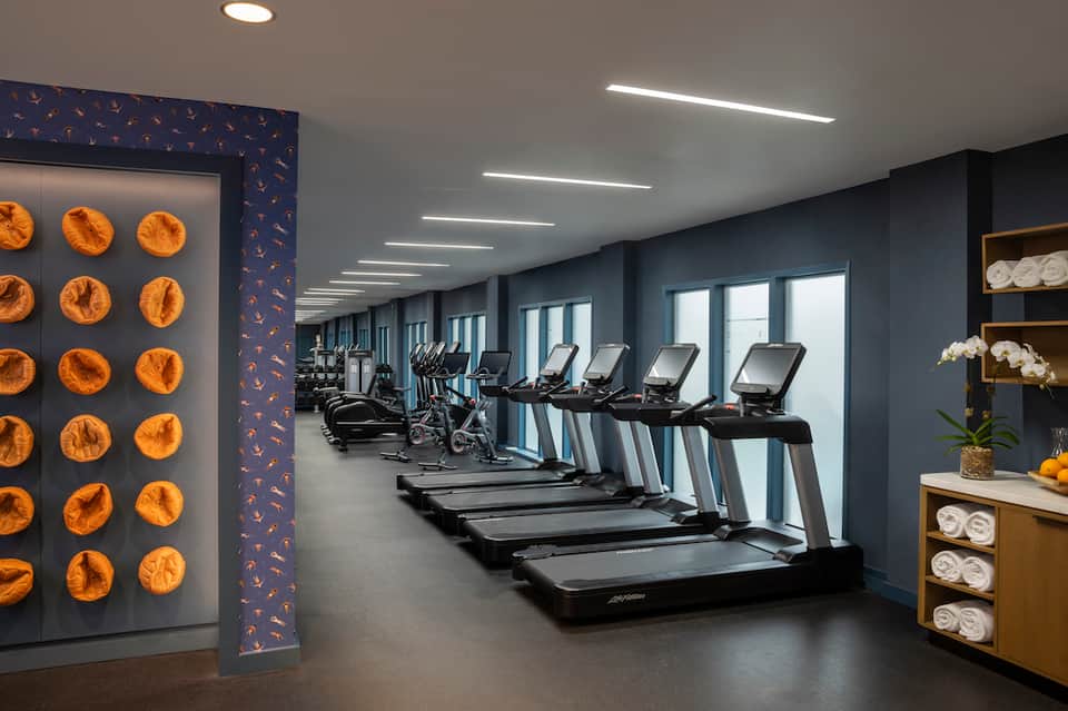 Modern fitness center with treadmills, orange citrus wall art, and large windows