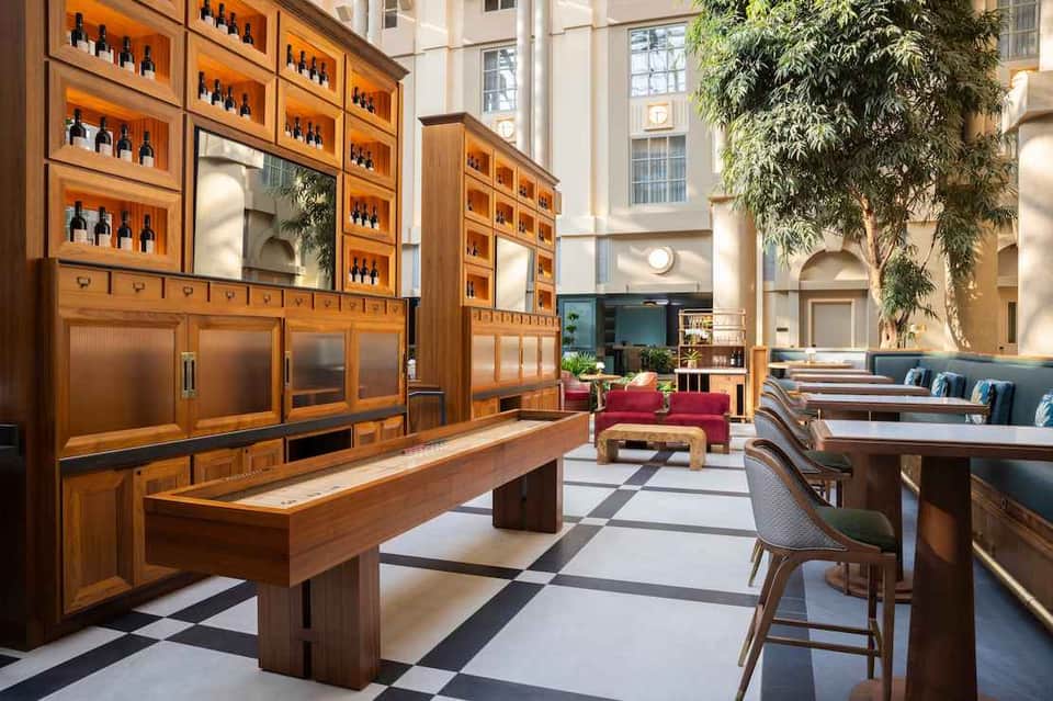 Upscale hotel lounge with wooden wine display cabinets, modern furniture, and natural light from high ceilings