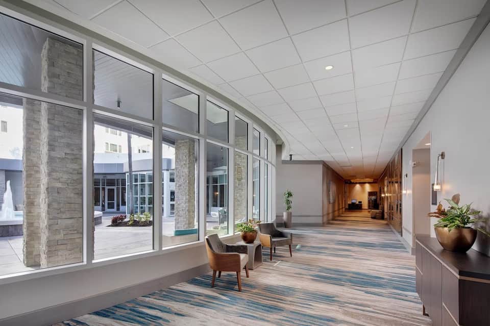 Bright hotel corridor with large windows, stone columns, wooden flooring, and contemporary interior design