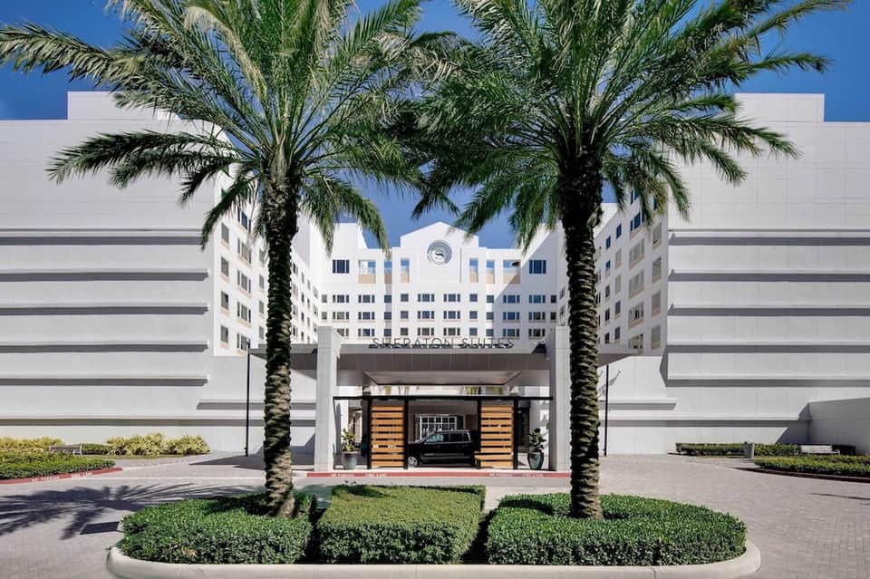 Hotel entrance with white modern architecture, palm trees, and covered portico