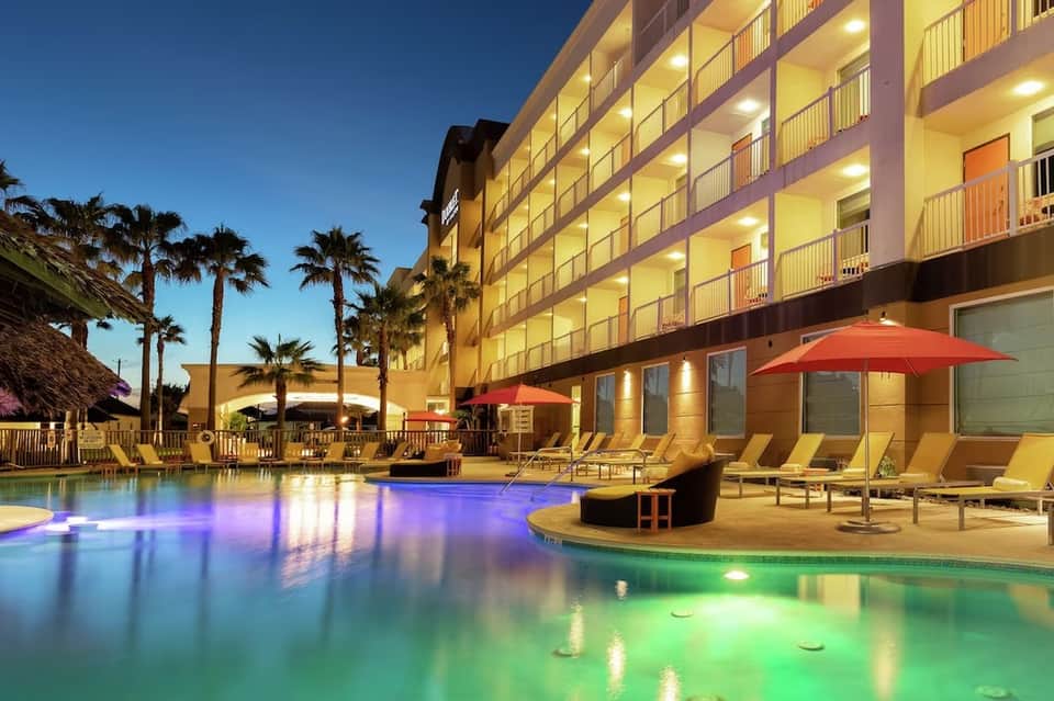 Illuminated resort pool at night with purple and green lighting and palm trees