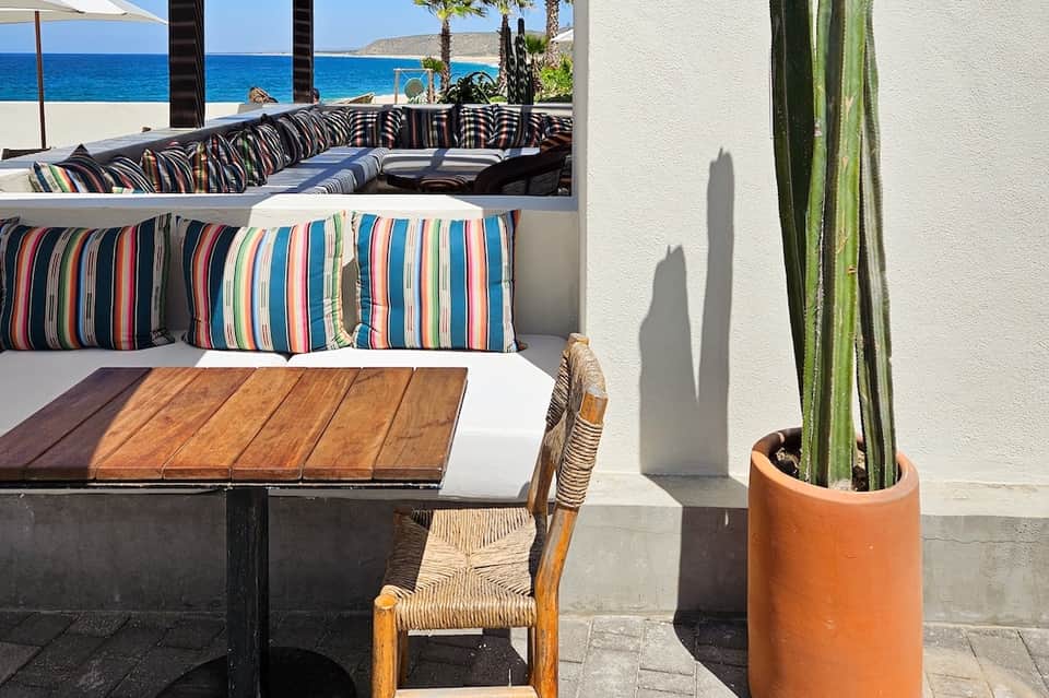 Beachfront lounge area with striped pillows on built-in seating overlooking ocean and blue sky