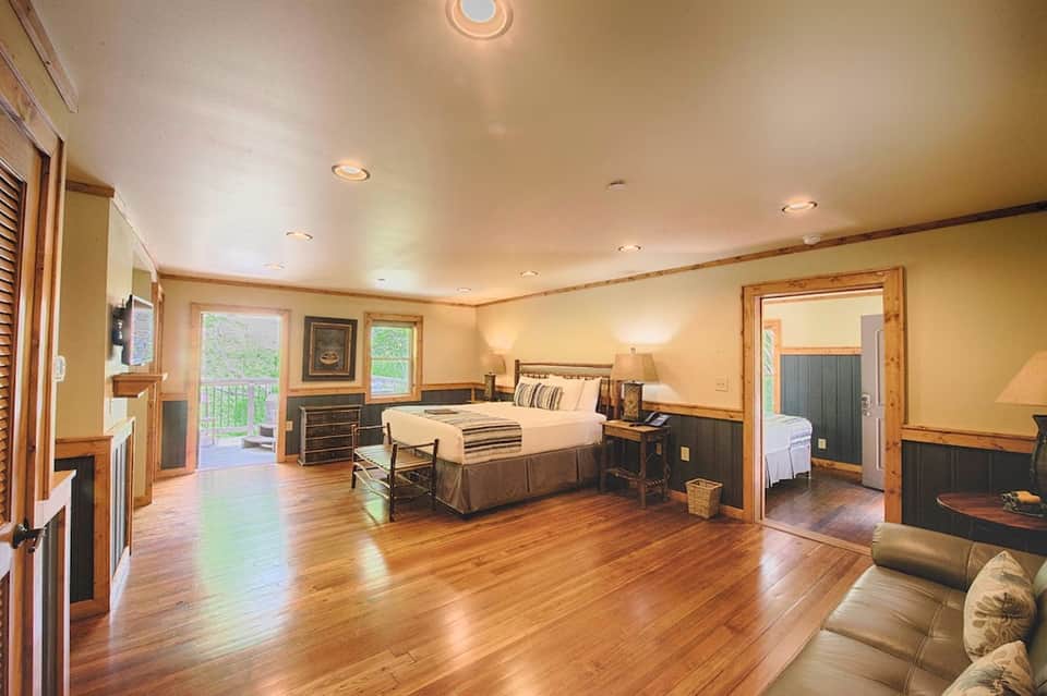 Spacious hotel suite with king bed, fireplace, wooden floors, and sliding glass doors to outdoor balcony